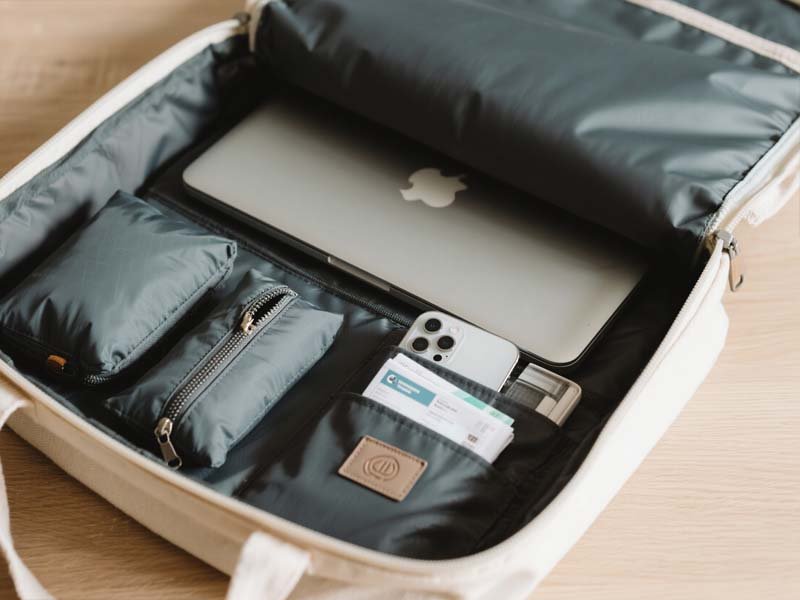 Open waterproof tote showing padded laptop sleeve, packing cubes, and travel essentials.