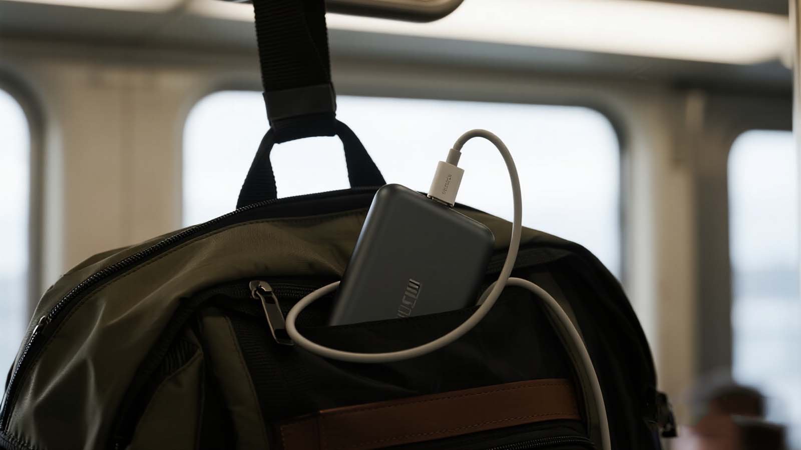 Backpack with side charging port and luggage strap secured to train overhead rack.