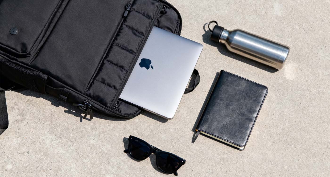 Durable Laptop Backpack: How to pick a tough pack that lasts - laptop bag flatlay of a durable laptop backpack with laptop, water bottle, notebook, and sunglasses on concrete background