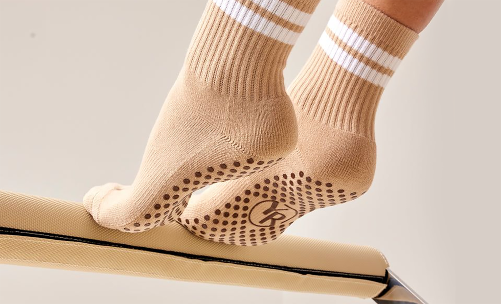 About Us - laptop bag Close-up of tan professional Pilates grip socks with white stripes, providing maximum stability on a reformer footbar.