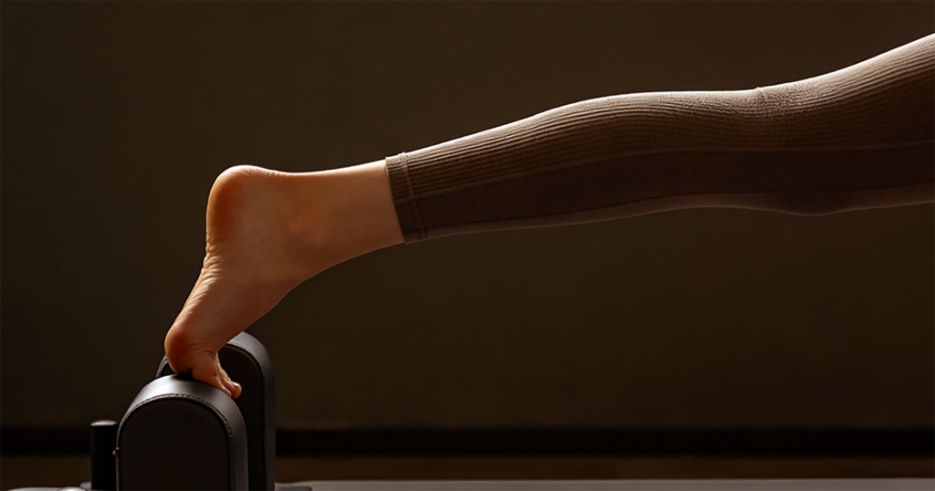 Home - laptop bag Bare foot struggling for grip on a Pilates reformer shoulder rest during a workout.